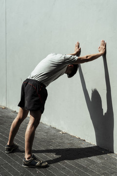 年轻强壮的男人伸出手，把手放在墙上，推着墙。运动前热身概念。