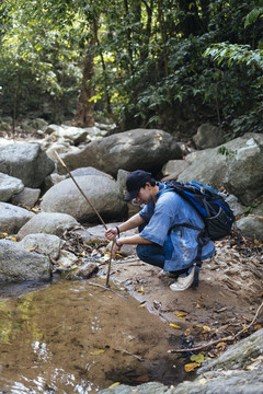 男性徒步旅行者在森林里有大石头的瀑布边休息。