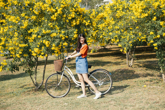 穿着橙色t恤和牛仔裤的长发女孩骑着自行车站在黄色的花园里。