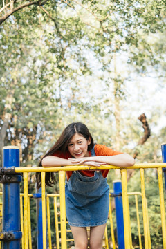 长发女孩穿着橙色t恤和牛仔裤跳投俯身在黄色扶手上的操场滑，垂直。