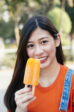 长发女孩穿着橙色t恤和牛仔裤套头衫展示橙色冰淇淋，特写。
