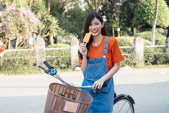 长发女孩穿着橙色t恤和牛仔裤套头衫，展示自行车上的橙色冰淇淋，水平。