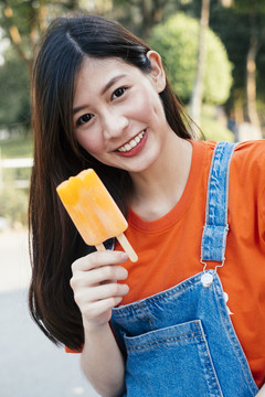 一张长发女孩的肖像照，她穿着橙色t恤和牛仔裤，还有她的冰淇淋。