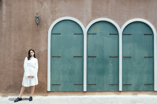 美丽的白衣长发女孩站在绿色门和灯的棕色墙前。