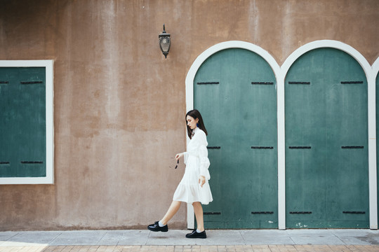 美丽的白衣长发女孩走在绿色门和灯的棕色墙壁上。