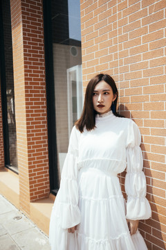 美丽的长发女孩穿着白色连衣裙站在阳光下的砖房，中镜头。