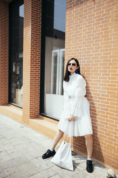 阳光下，美丽的长发白衣女孩站在砖房前，双腿宽阔。