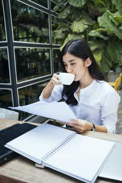 办公室工作的女人喝着咖啡，读着文件，坐在木桌上。
