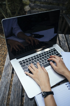 办公室的女人在户外花园里操作笔记本电脑键盘。