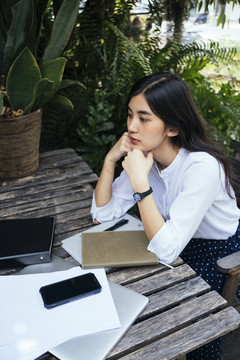 体贴的年轻亚洲办公室工作妇女坐在木桌旁的椅子上，面前摆着一堆工作。