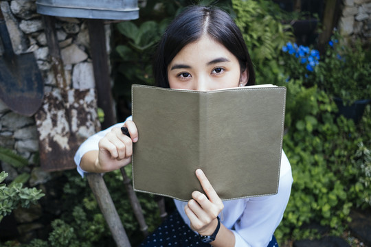 害羞的亚洲女孩躲在书后面，用可爱的眼睛看着相机。