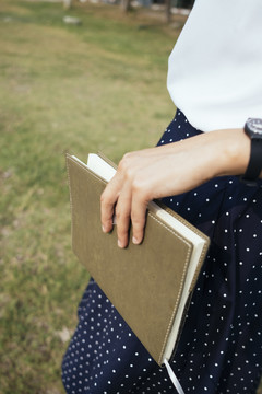特写照片中的女人拿着一本书，站在秋天的草地上。