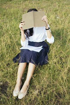 坐在草地上的年轻女子用一本书遮住脸。