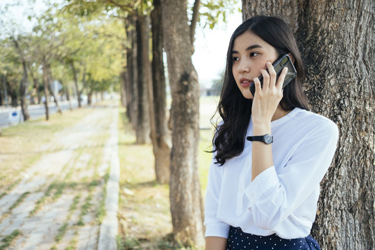 一个穿着白衬衫的亚洲女人在打电话，和朋友聊天。