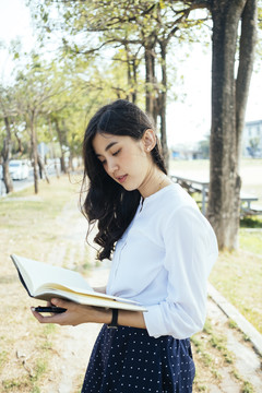 秋天，穿着白衬衫的亚洲女人在公园看书。