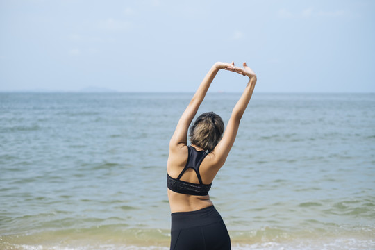 短发运动型女人在沙滩上伸展和做瑜伽，伸展手臂并向右倾斜。