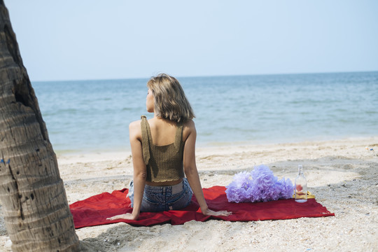 夏天，短发女孩坐在沙滩上的红垫子上。