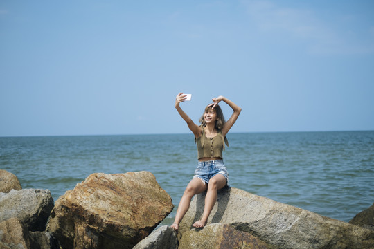 短发女孩站在沙滩上，坐在海边的岩石上自拍。