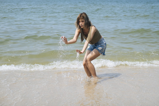 短发女孩穿着短牛仔裤喜欢在沙滩上散步，喜欢大海和海浪，赤脚。