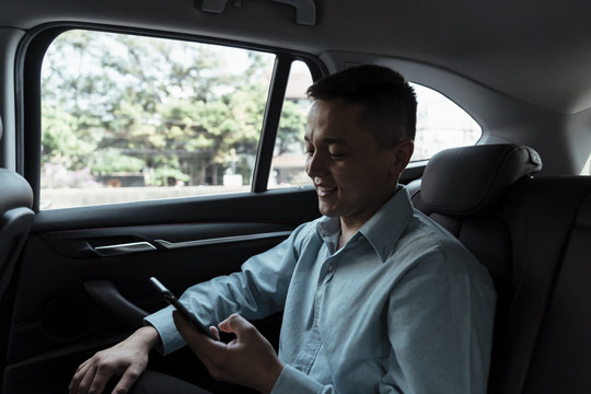 穿着蓝色衬衫的商人坐在汽车后座上，他微笑着从电话里得到好消息。