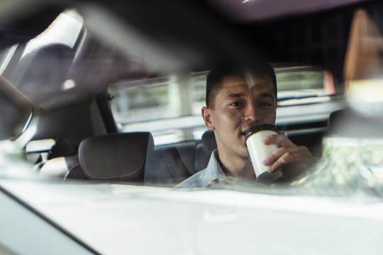 从后视镜中可以看到商人在开车去办公室时喝咖啡的情景。