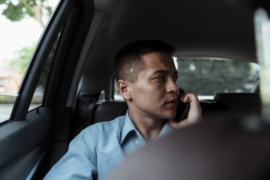 在汽车后座穿着蓝色衬衫的商人在旅行中使用电话。