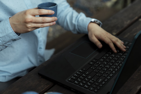 一个男人手里和笔记本电脑里模糊的茶杯的剪影。