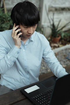 穿蓝色衬衫的黑发男子在工作时接到顾客的电话。