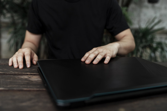 一个穿着黑色t恤的男人面前的木桌上，一个被剪掉的笔记本电脑的图像。