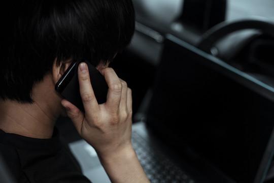 一个穿黑色t恤衫的男人在开车回家时接到一个电话，他又打开了笔记本电脑。