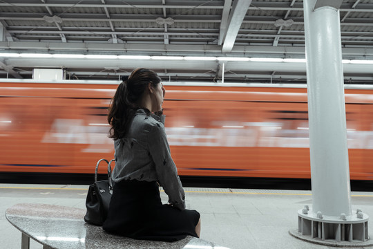 后视图-亚泰妇女等待火车回家在曼谷的火车站台在晚上。