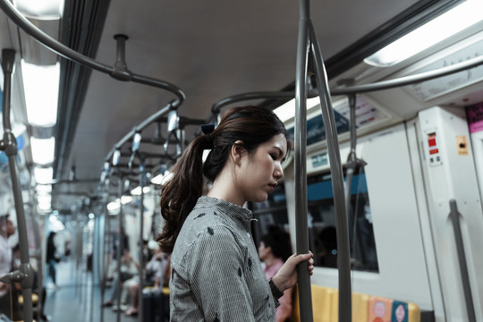 一名亚泰妇女站在火车上抓着一根杆子准备回家。