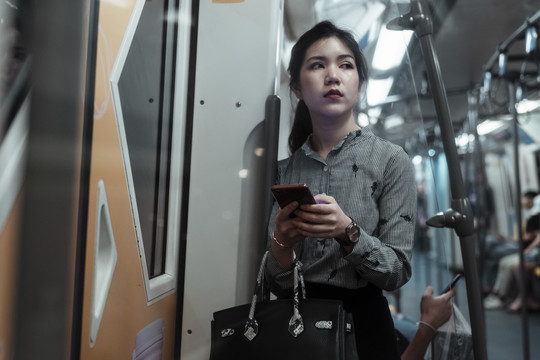疲惫的亚泰妇女晚上在火车上使用智能手机。