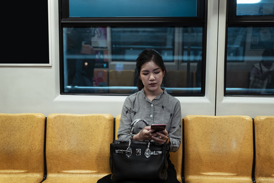 坐在火车黄色椅子上使用智能手机的亚泰妇女。