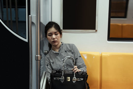 疲惫的亚泰妇女坐在火车上睡觉的黄色椅子上。