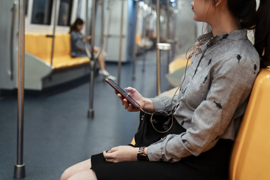 侧视亚泰妇女坐在黄色椅子上用智能手机听音乐耳机内的列车。