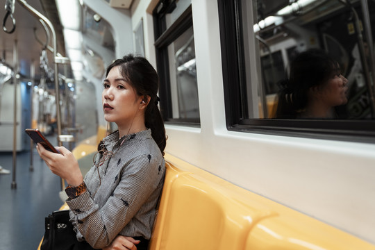 复制空间-亚泰妇女坐在火车上用智能手机耳机听音乐。