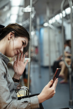 亚泰妇女在火车上用智能手机打视频电话的侧视图。