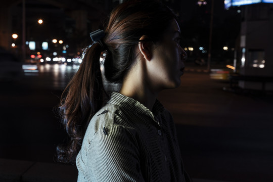 侧视特写-晚上站在街上的女人。