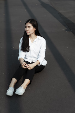黑发女人穿着白衬衫坐在阳光下的黑地板上。