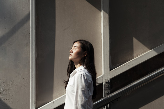 在强烈的阳光下，泰国妇女站在建筑物结构的墙上的肖像。