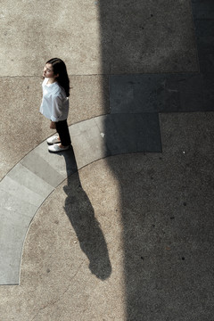 阳光下，穿着白衬衫的女人站在广场的鹅卵石地板上的俯视图。