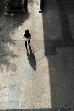 白衣女子在阳光下走向广场大门的俯视图。