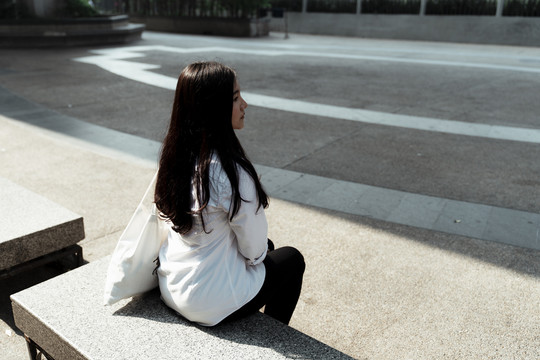 坐在广场上晒太阳的女人的背影。
