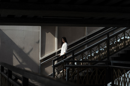 一个女人走下桥的楼梯，走向夏日的阳光。