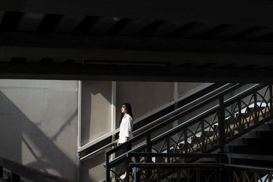 一个女人走到桥的楼梯边，直视着阳光。