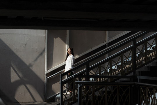 在夏日的阳光下，站在楼梯尽头的黑发白衬衫女人。