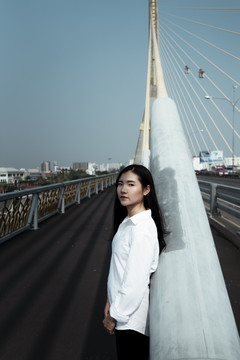 长长的一张照片，在大风天，一个穿着白衬衫的黑发女人靠在桥上巨大的白色吊带上。