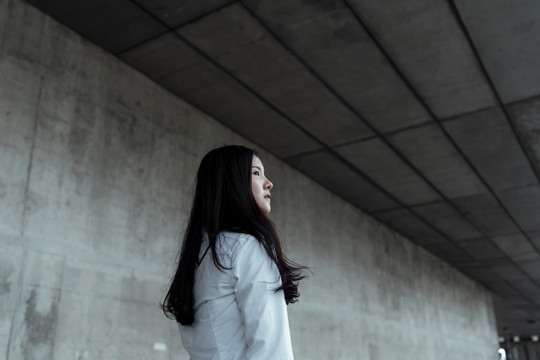 身穿白衬衫的黑色长发女子站在阁楼式建筑前，领头线朝上。