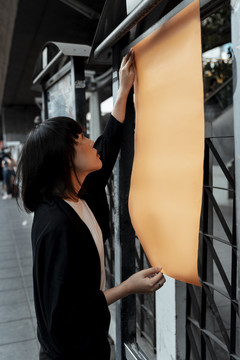 年轻的泰国亚裔女子深色短发站在街上橙色的空白纸上。